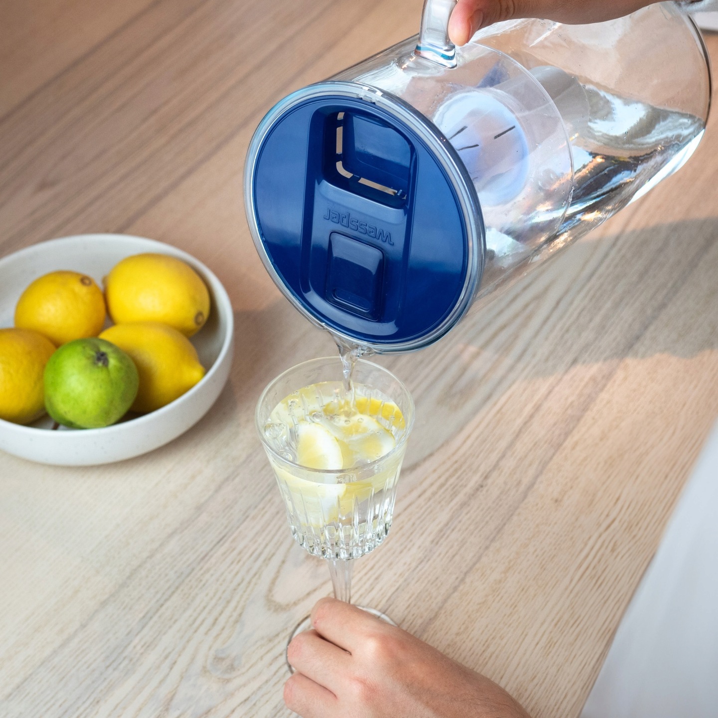 Kobieta nalewa czystą przefiltrowaną wodę z&nbsp;dzbanka Wessper do szklanki